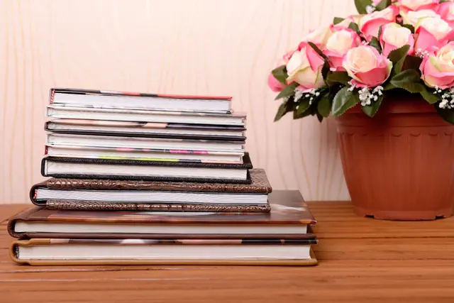 Teanc de albume foto pe o măsuță, lângă un ghiveci cu trandafiri