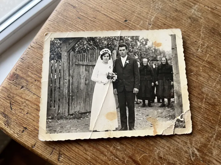 O fotografie veche de nuntă, ruptă și pătată, așezată pe o masă de lemn